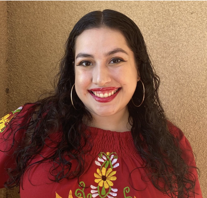 A Latinx woman with a red shirt and long brown hair smiling into the camera.