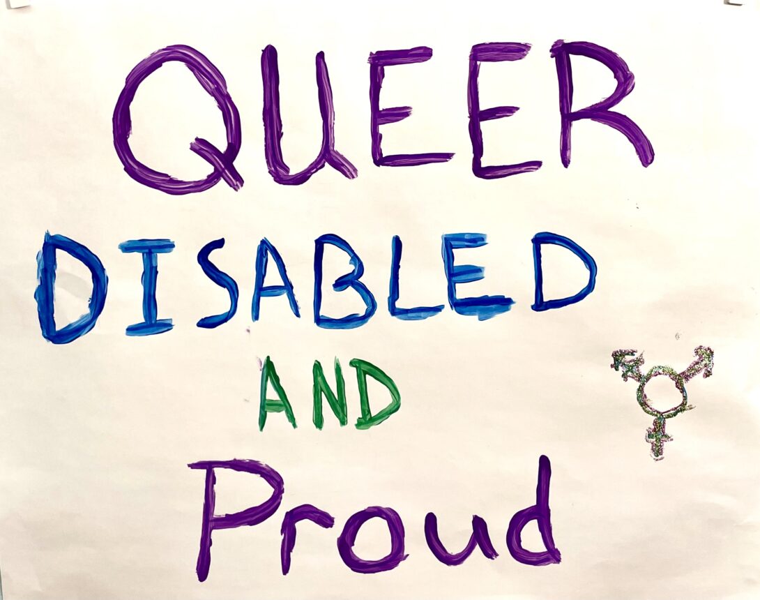 A white poster with the words “Queer Disabled and Proud” with  queer and proud in dark purple paint, disabled in dark blue paint, and the word and in green paint. There is a transgender pride symbol drawn in silver glitter in the bottom right corner.